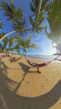 Dikey video. Hamak Palm Trees 'e Bağlı Kum Tropikal Sahili' nin üzerinde dinlenen adamla 360 Derece Geniş Açı Bakış Açısı Yakalandı