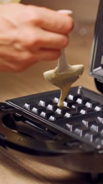 Dikey video. Yavaş Çekim Kaşık Kalın Vurucuyu Açık Waffle makinesine dökerek Mutfak tezgahına Dikkatli Yemek Hazırlama ve Pişirme Sürecini Gösteriyor