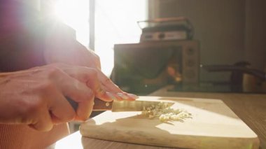 Sunlit Kitchen 'da, sarımsağı bıçakla doğrayan kadının yavaş çekimi, dikkatli yemek hazırlığını gösteriyor.