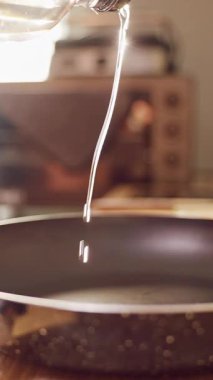 Dikey video. Yavaşça yağın şişeden tavaya dökülmesi mutfak tezgahında sıcaklıkla yemek pişirmeye hazırlanması.