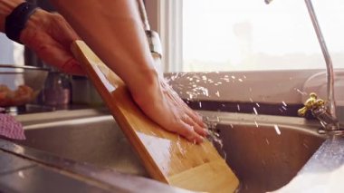 Mutfak lavabosunda akan suyun altında ahşap kesme tahtasının yavaşça durulanması Yemek pişirme işleminden sonra temizlik sürecini gösteriyor