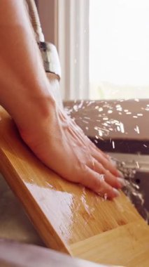 Dikey video. Mutfak lavabosunda akan suyun altında ahşap kesme tahtasının yavaşça durulanması Yemek pişirme işleminden sonra temizlik sürecini gösteriyor