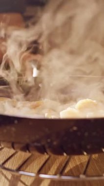 Dikey video. Yavaş çekim, tavadaki buharlı karides fırından çıkarıldı ve güneş ışığıyla aydınlanan mutfakta metal bir rafa kondu ve sıcak ev yemeği pişirme havası yarattı.