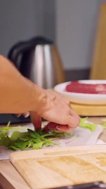 Dikey video. Mutfakta taze yeşil yaprakları düzenleyen kadın elleri, sağlıklı beslenme ve ev yemeği hazırlama.