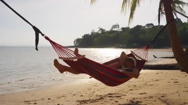 Hamakta yatan kadın, güneş ışığının suya yansımasıyla, huzurlu tropikal kaçış ve kıyı yaşam tarzıyla