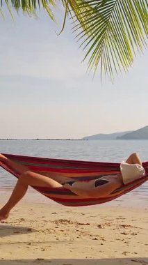 Dikey video. Yumuşak dalgalar ve palmiye gölgesiyle Hamak 'ta uzanan Kadın, Sakin Tropikal Öğleden Sonra Keyfi