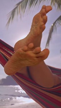 Dikey video. Kum ile kaplı çıplak kadın ayakları Tropikal sahilde dinleniyor Palmiye ağaçları ve yumuşak akşam ışığı ile