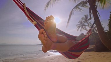 Kumlu Çıplak Ayaklar 'ın Hamakta Rahatlarken, Arka planda Okyanus ve Palmiye Ağaçlarının Sakin Tropikal Ortam Oluşturuşunun Yakın Görüntüsü