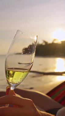 Dikey video. Gün batımında Hamakta, Tropikal Sahilde Elde Şampanya Kadehi Romantik Tatil Atmosferi Oluşturdu