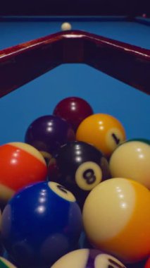 Dikey video. Mavi masadaki saçılmış bilardo topları dramatik bir şekilde düşük ışıkta çekilmeye hazır.