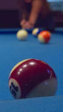 Dikey video. Kırmızı ve beyaz bilardo topunu yakın plan çekimleri için hazırlanan bir kadınla mavi masaya koyun.