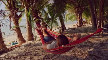 Hamaktan, tropik plajın yakınındaki palmiye ağaçlarının altında uzanan ilk kişi rahatlama hissi yaratıyor.