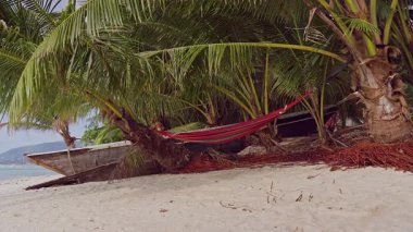 Kumsalın yukarısındaki Palmiye ağaçlarının arasındaki boş hamak Sakin Okyanus Rahatlama Sembolü Oluşturur