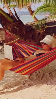 Dikey video. Hamak 'ta, Palmiye Ağaçları ve Sakin Tropikal Deniz' le Birlikte Dizüstü Bilgisayarda Çalışan Kadın Geniş Görüş