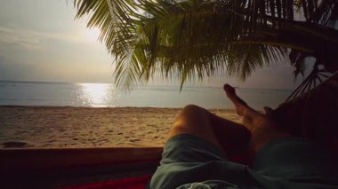 Hamakta dinlenen ilk insan görüntüsü Palm Palm Beach 'in altındaki kum tropikal plajlarda sakin deniz ve ılık ışık altında huzurlu bir tatil ve yavaş bir yaşam ortamı yaratıyor.