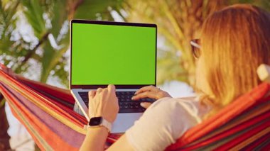 Palmiye ağaçlarıyla çevrili hamakta dizüstü bilgisayarlı bir kadın Mobil Ofisi ve Uzaktan Kariyer Yaşam Tarzı Gösterme Omuzunda