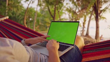 Palm Trees 'in Altında Dinlenen Hamak' ta Yeşil Ekranlı Dizüstü Bilgisayarı İşleyen Kadın, Esnek Çalışma ve Seyahat Yaşam Tarzı Gösteriyor