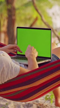 Dikey video. Hamak Kıyısı 'nın yanındaki Hamak' ta Yeşil Ekran Kadın Bacakları Üzerine Dizüstü bilgisayar, İlk Kişi Görünümü Yaşamın Her yerinden Çalışmayı Gösteriyor