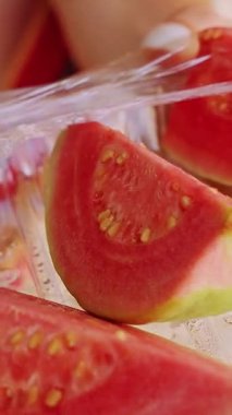 Dikey video. Plastik kabın içinde taze dilimlenmiş Guava 'ya yaklaş. Tropikal meyve dokusunu ve sağlıklı atıştırmalık detaylarını göster.