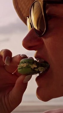 Dikey video. Tropikal Sahilde Macaron Yiyen Kadın Rahatlamış Tatil ve Tatlı Şımarıklık Sahnesi