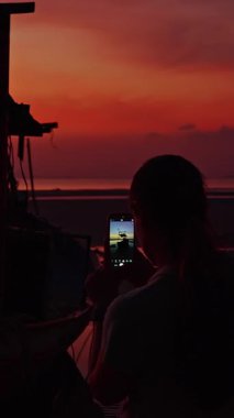 Dikey video. Sunset, Siluet Sahnesi, Sıcak Akşam Renkleri, Seyahat Belleği ve Gözlemlemedeki Akıllı Telefonlu Balıkçı Teknesi