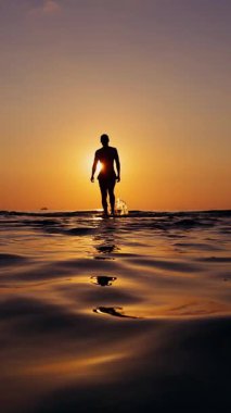 Dikey video. Deniz 'de Yürüyen Yalnız Kişinin Geniş Açı Manzarası Gün batımına doğru Merkezli Silüet ve Suyun Ilık Yansıması Yol Gösterme Süreci ve Kişisel Yolculuk