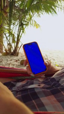 Dikey video. Tropikal Sahilde Palmiye ağaçlarıyla dinlenirken Mavi Krom Anahtar Ekranlı Kadın El ele tutuşan Akıllı Telefonun Görüntüsünü Kapat