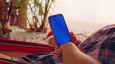 Palmiye Ağaçları Arasındaki Hamakta Dinlenen Kadın tarafından kullanılan Mavi Model Ekranlı Akıllı Telefon Dijital Özgürlük ve Mobil Yaşam Tarzını Temsil Ediyor
