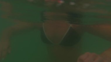 Tropikal kıyılarda sakince yüzen bir kadın, arkada orman sahili olan su seviyesi, sakin, yavaş çekim okyanus yaşam tarzı.