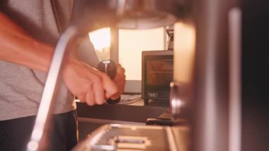 Modern mutfak içinde el yapımı öğütücüyle kahve çekirdeği öğüten adam, Sıcak Günbatımı Işığı ve Yavaş Hareket sakin bir kahve demleme havası yaratıyor.