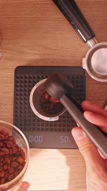 Dikey video. Espresso Hazırlık sırasında 18 gramlık dijital ölçekte kahve çekirdeğini ölçen adam, Sıcak Işık ve Yavaş Hareket ile Üst Görünüm barista el akışını gösteriyor