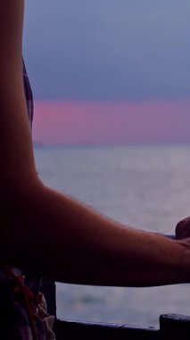 Dikey video. Gemi güvertesinde duran kadın sakin denizde yelken açarken tırabzanı tutuyor. Yolculuk ruh hali yansıması ve sessiz okyanus yolculuğu yaratıyor.