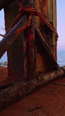 Dikey video. Düşük açılı paslı metal desteği ve kıyı rıhtımında deniz ve kayalıklarla örülmüş deniz yapısı ve sert okyanus ortamını gösteriyor.