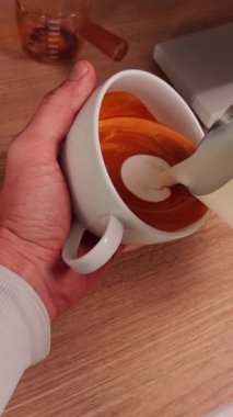 Dikey video. Süt akıntısı Espresso yüzeyi ile harmanlanır. Barista beyaz kupa içinde Latte sanatını bitirir. İlk bakışta pürüzsüz hareket ve kremsi doku.