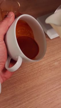 Dikey video. Espresso Kupasına dökülen sütün ilk insan görüntüsü ahşap tezgahta pürüzsüz girdap deseni, ev yapımı barista tatbikatı ve Latte sanat eğitimi yaratıyor.