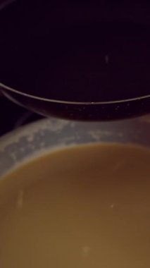 Dikey video. Loş Mutfak Işığı, Ev Yapımı Krep Pişirme ve Akşam Yemeği Hazırlama 'da Işıl ışıl yanan elektrikli ocağın üzerine kepçe döken vurucuyu kapatın.