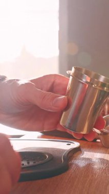 Dikey video. Sıcak Güneş Işığı Erkek El 'in Metal Kaptaki Taze Kahve' yi Dijital Ölçek ve Fasulye Kavanozu, Ev Espresso Ritüeli ile filtre sepetinin üstüne koymasını aydınlatıyor.