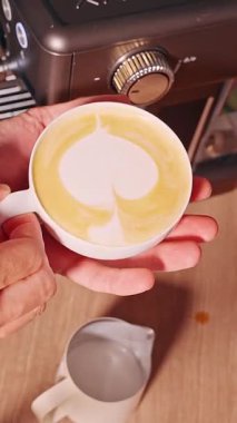 Dikey video. Ahşap Masa, Romantik Kahve Anı ve Ev Kahvesi Sanatı 'nda Erkek Elleri Latte Bardağı Kalple Şekillendirilmiş Süt Köpüğü Makinesi