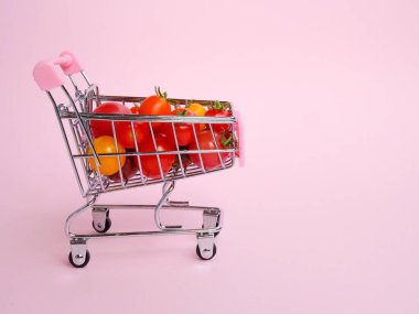 Pembe arka planda domateslerle dolu pembe alışveriş arabası.