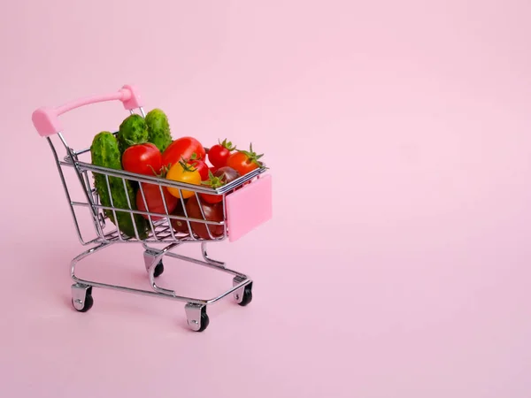 Carrinho de compras rosa cheio de legumes no fundo rosa — Fotografia de Stock