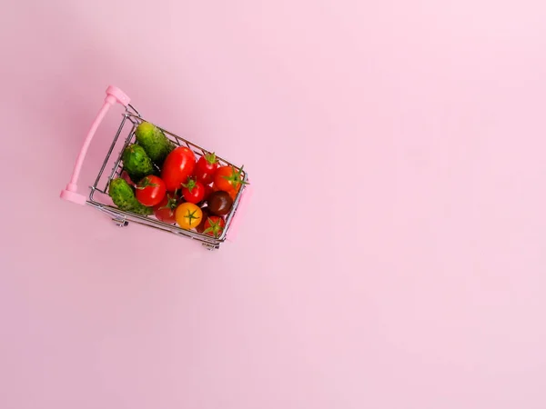 분홍색 배경에 야채가 가득 한 분홍색 쇼핑 카트 — 스톡 사진