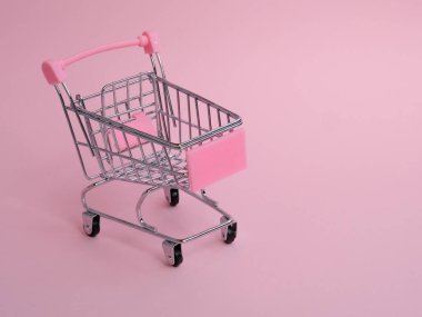 Pembe arka planda büyük salatalıklı küçük bir alışveriş arabası.