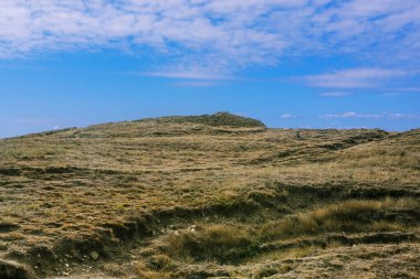 Tepe arazisi ve mavi gökyüzü. Dağ tepesi ve yürüyüş patikası. Tırmanmak ve dağlara seyahat etmek. Etkin turizm.