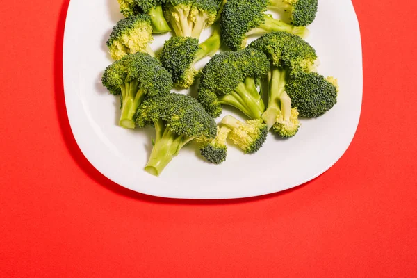 Broccoli Vit Tallrik Broccoli Kvistar Närbild Med Kopieringsutrymme Röd Bakgrund — Stockfoto