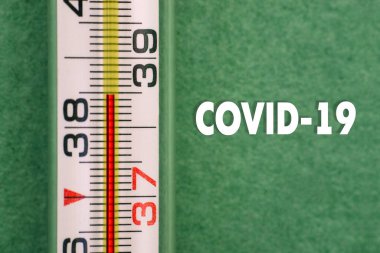 Yüksek sıcaklıktaki termometreyi COVID-19 metni ile kapatın. Koronavirüs hastalığı belirtileri. Virüs belirtileri. Vücut ısısı kontrolleri.