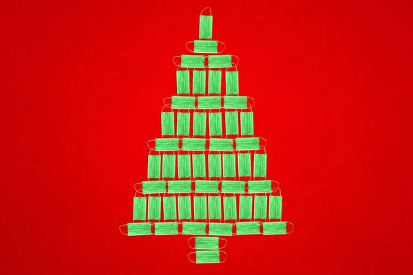 Noel ağacı. Tek kullanımlık tıbbi maskelerin kırmızı arka planında duran bir Noel ağacı figürü. Koronavirüse karşı koruma, covid-19. Yeni yıl kavramı.