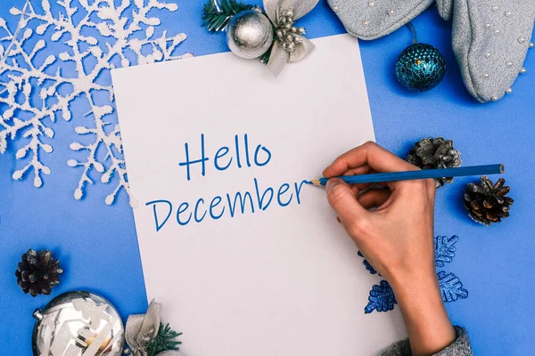 Merhaba Aralık. Kızın eli metni beyaz bir sayfa kağıda yazıyor. Noel kompozisyonu.