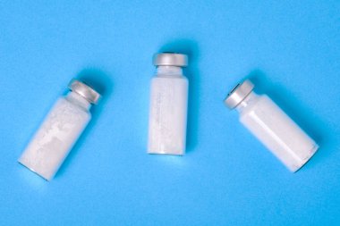 Mavi arka planda kovid ilaç bulunan cam şişe. Coronavirus aşısı. Virüs ve enfeksiyon koruması. Aşıların geliştirilmesi ve aşılanması.