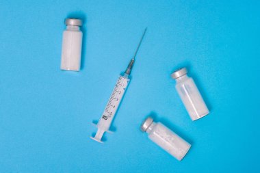 Beyaz tozlu cam ampul ve mavi arka planda plastik şırınga. Hastalıkların, enfeksiyonların ve koronavirüsün tedavisi için antibiyotik. Covid-19 aşısı. Tıp arkaplanı.