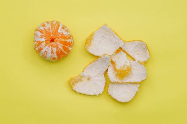 Sarı arka planda soyulmuş mandalina. Olgun mandalina ve kabuk. C vitaminli sağlıklı meyveler.